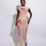 A model wearing an asymmetric top with a multicolored print and matching pants, standing against a white background.