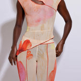 A model wearing an asymmetric top with a multicolored print and matching pants, standing against a white background.