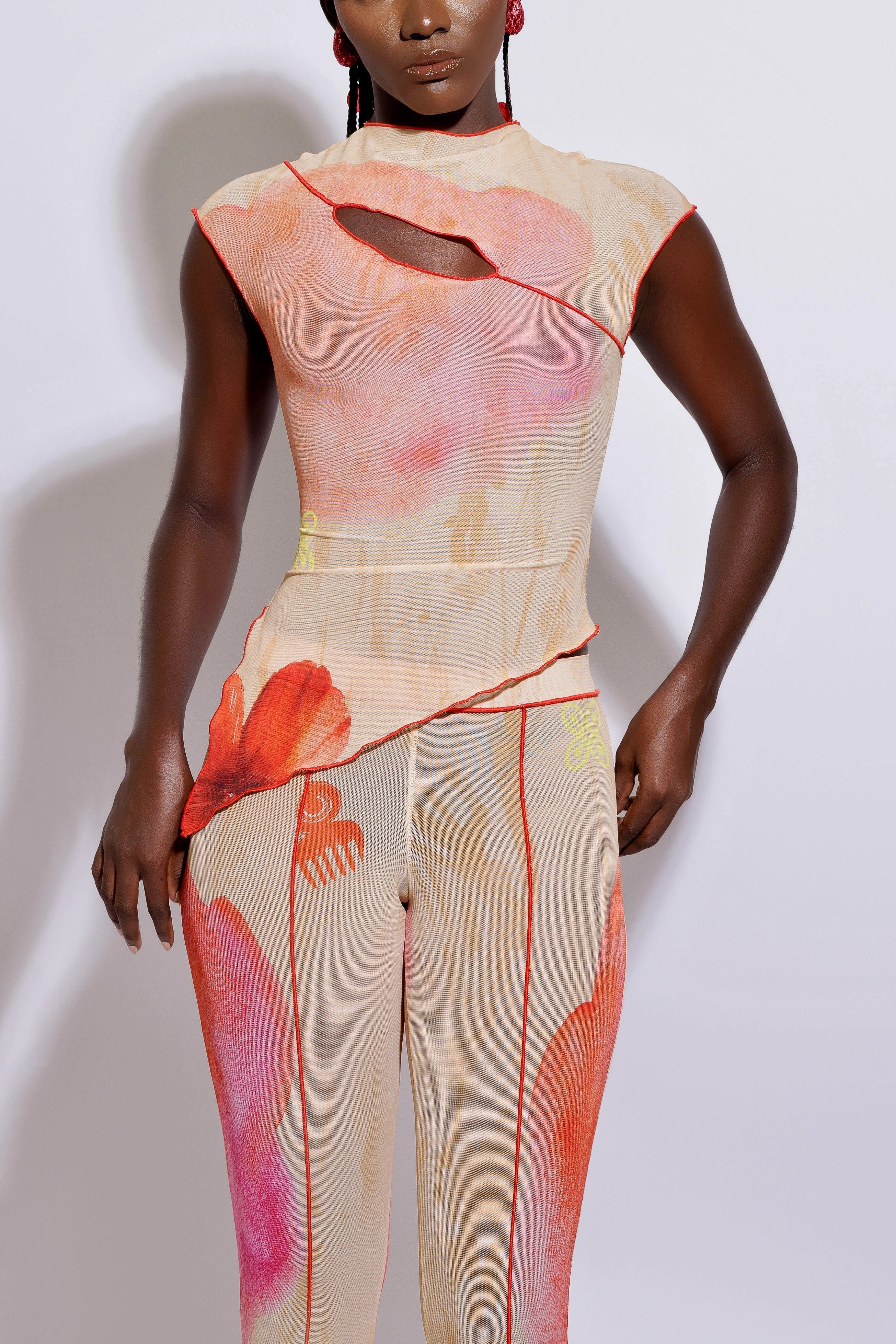 A model wearing an asymmetric top with a multicolored print and matching pants, standing against a white background.