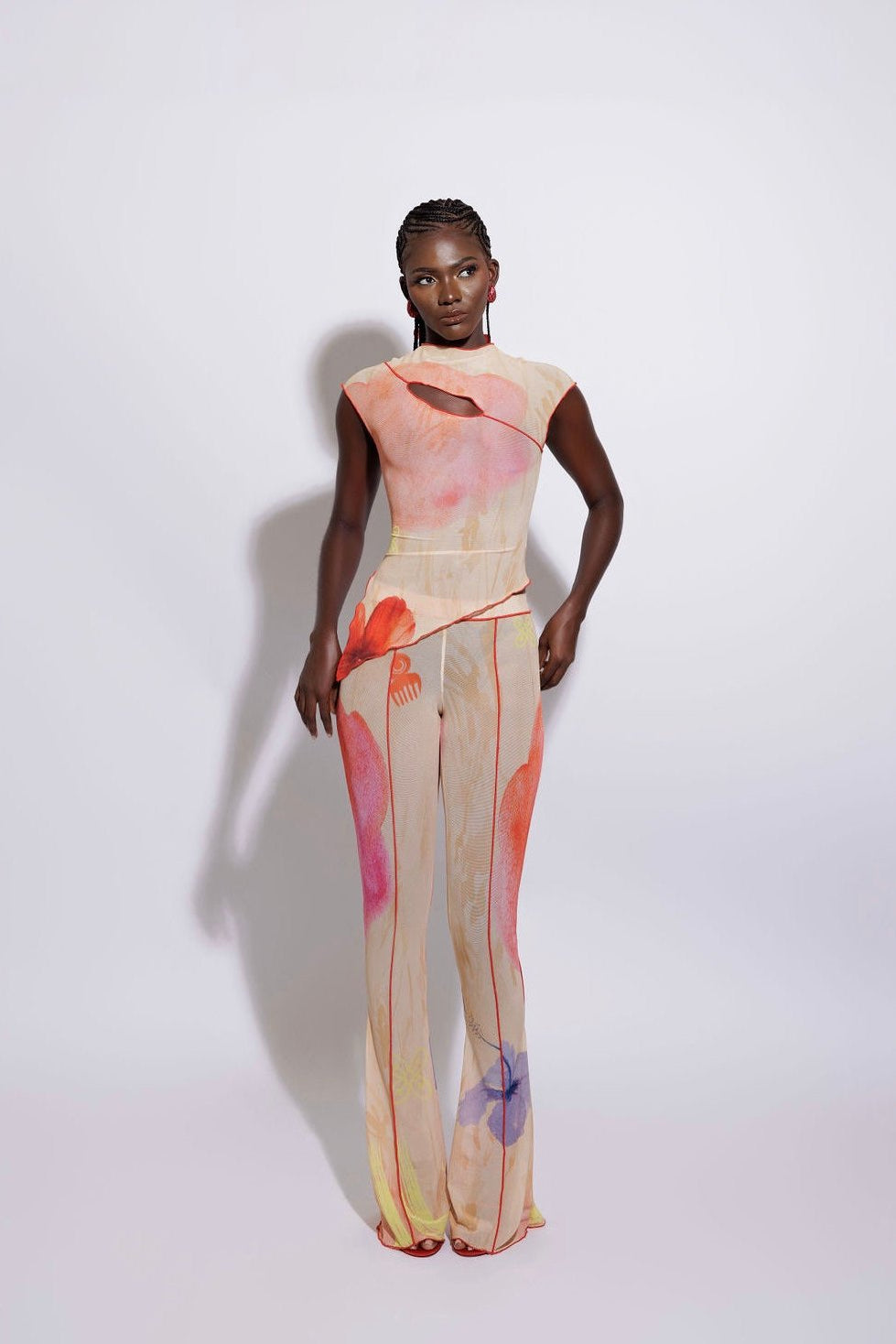 A model wearing an asymmetric top with a multicolored print and matching pants, standing against a white background.
