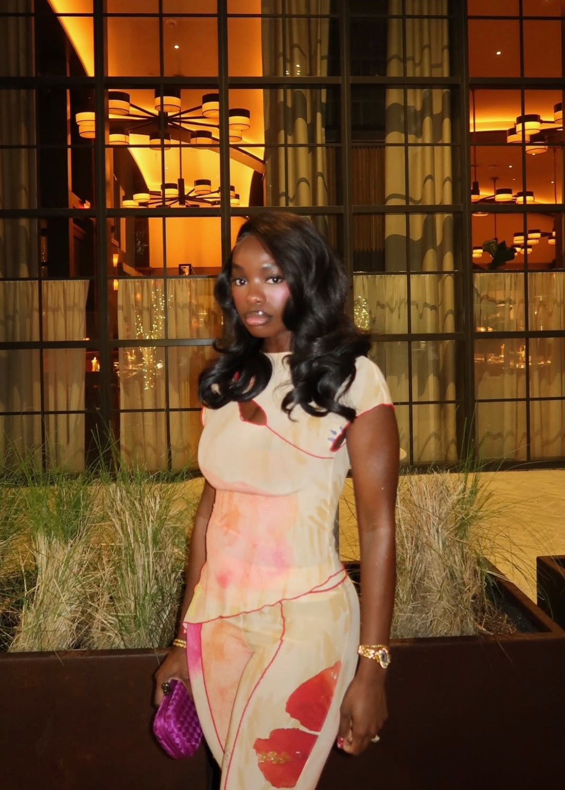 Woman in a patterned outfit standing in front of a building with large windows.