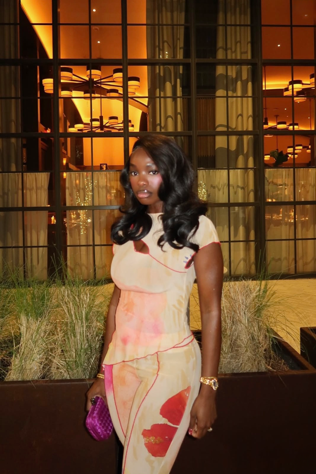 Woman in a patterned outfit standing in front of a building with large windows.