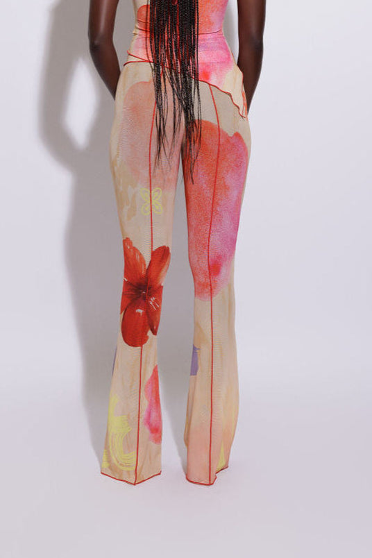 A model wearing flared mesh pants with a floral pattern, viewed from the back.
